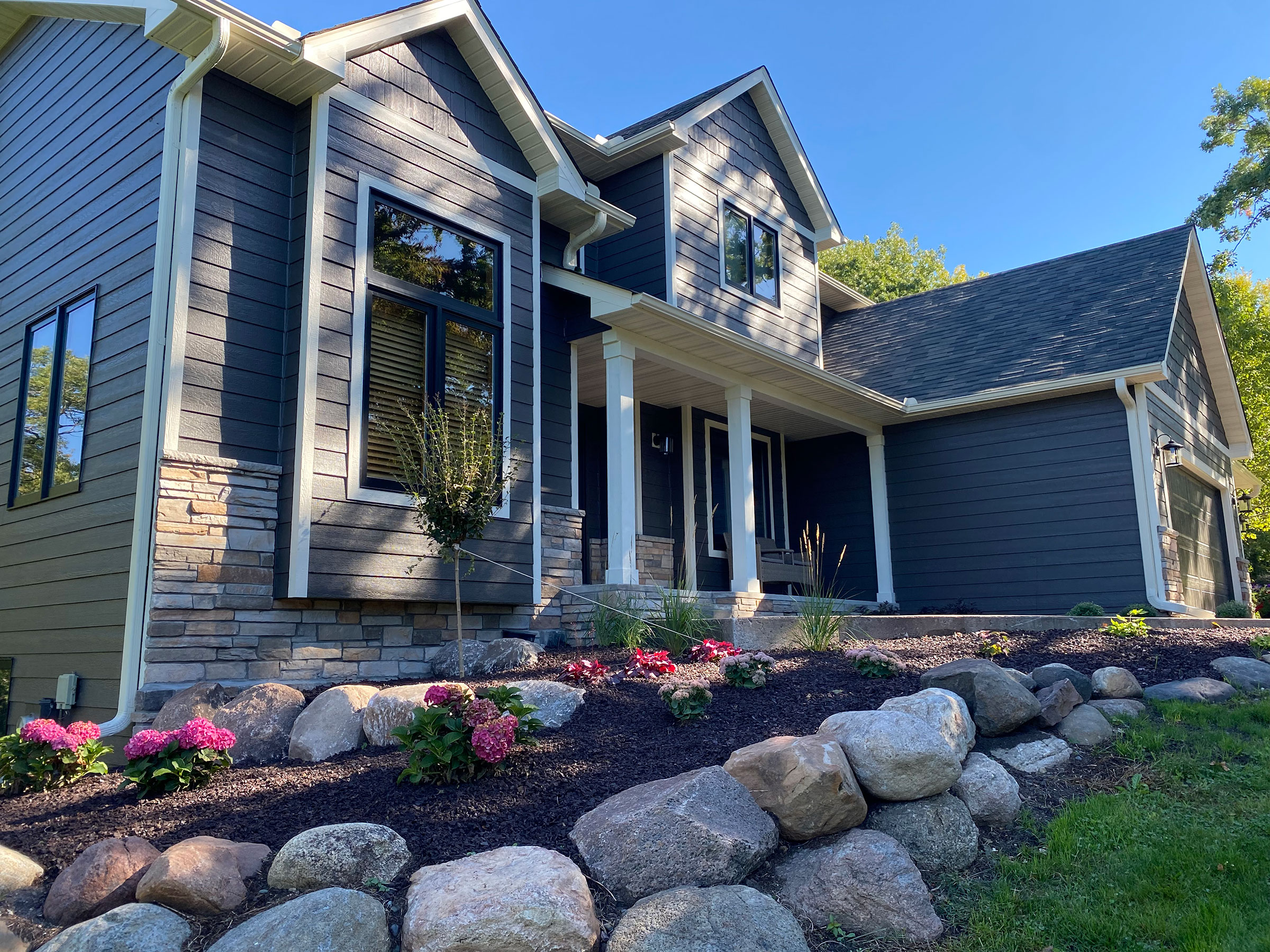 A finished blue two-story home with fresh landscaping and stone edging