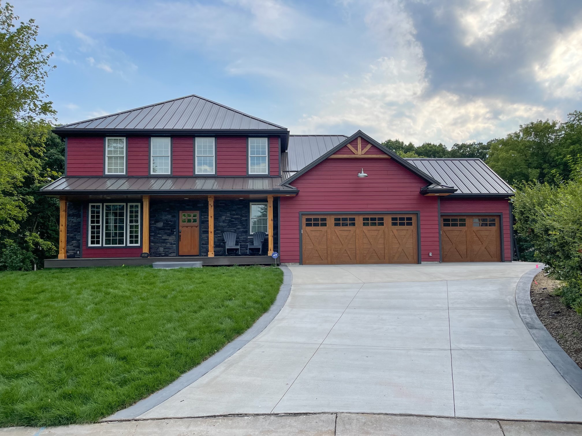 A red two-story home with a black standing-seam metal roof and a wide concrete driveway