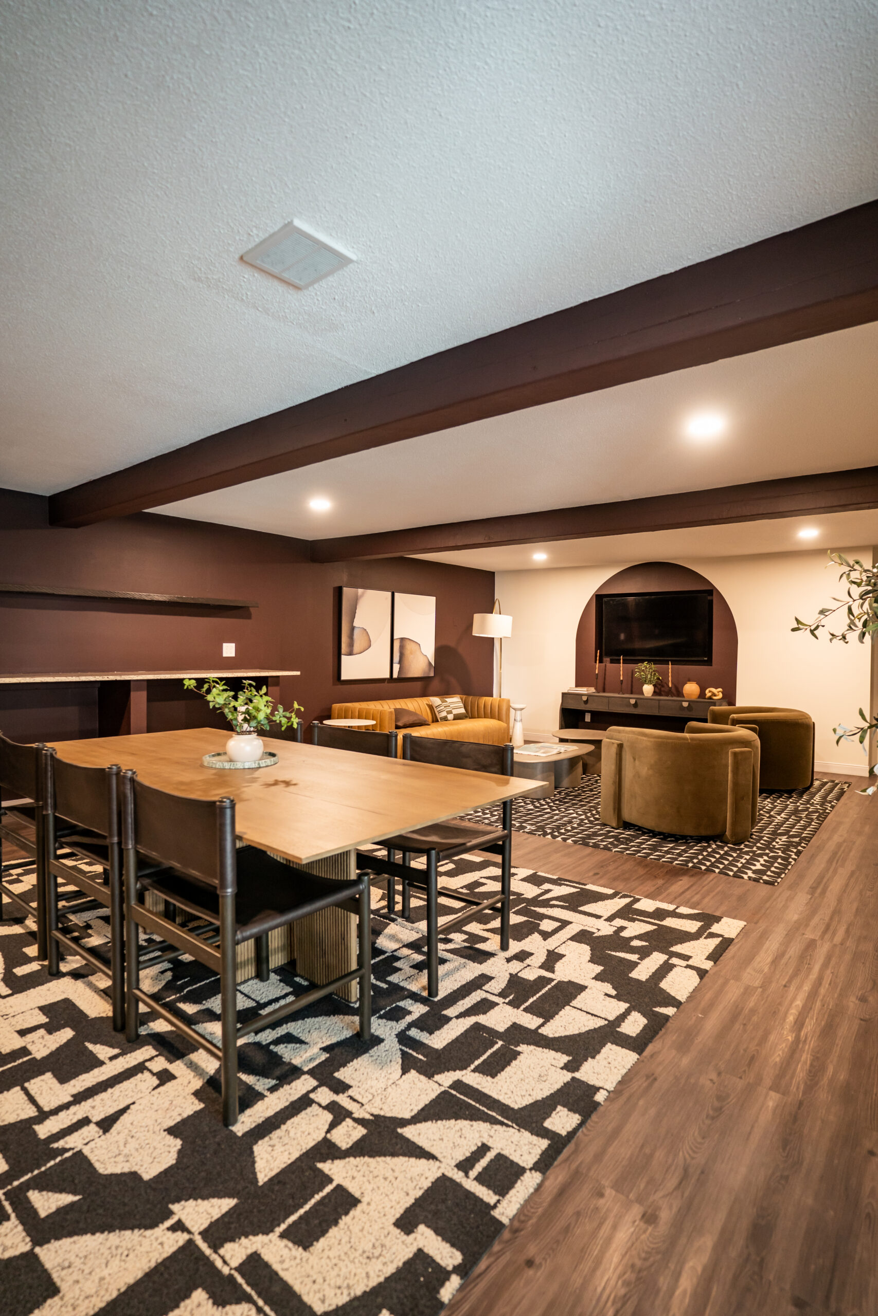 A finished open-concept great room remodel with warm wood ceiling beams, a dining area and a living room