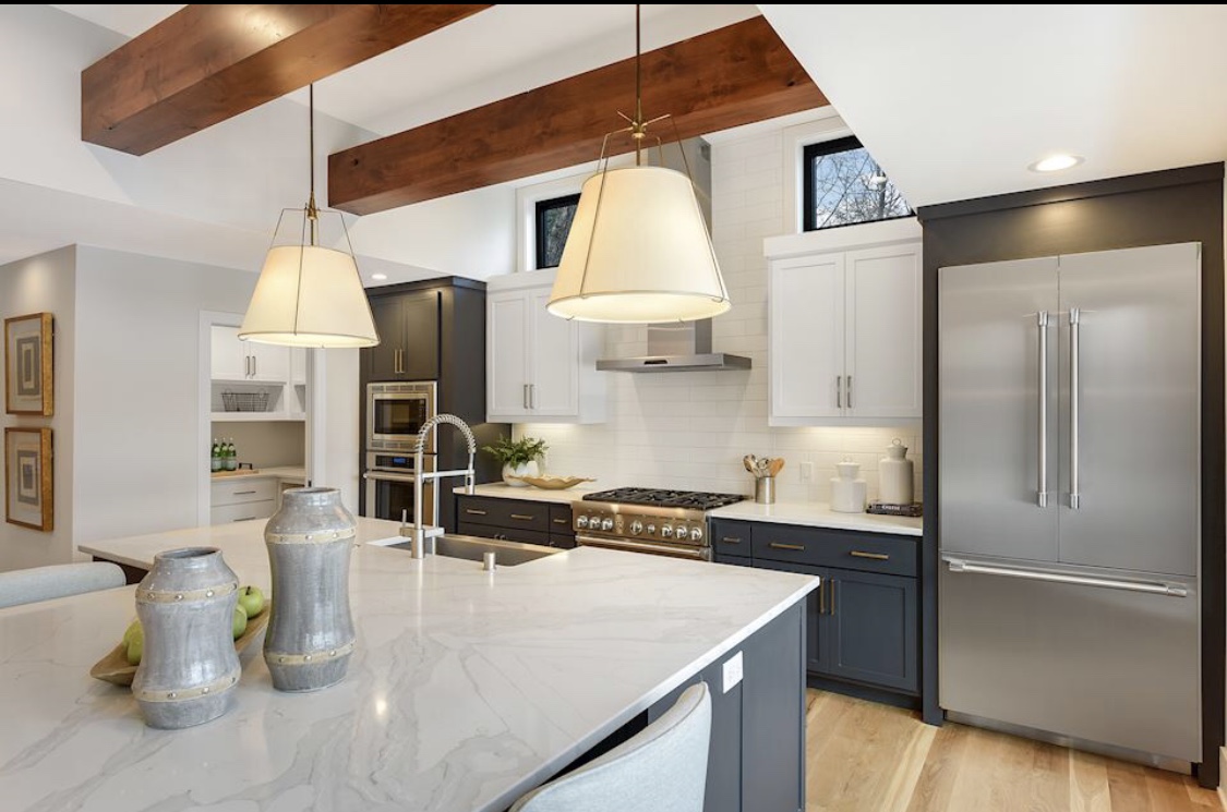A bright kitchen with a marble-topped island, stainless appliances and wood ceiling beams