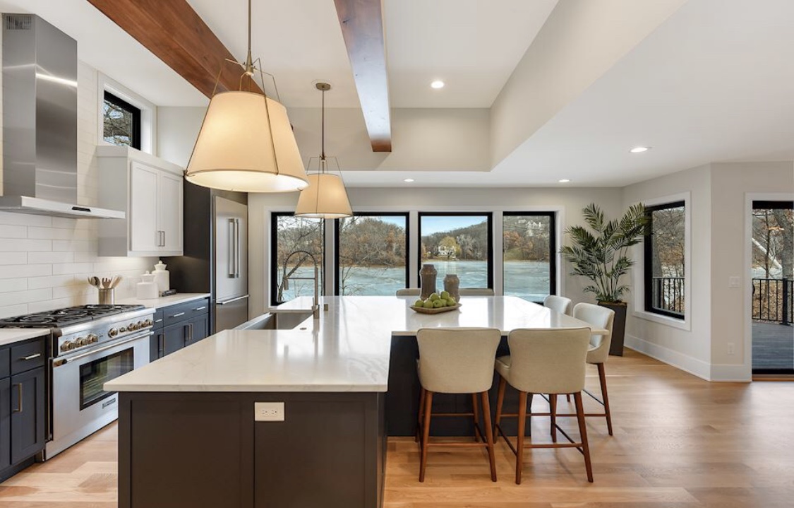 A finished kitchen remodel with a large island, bar seating, wood ceiling beams and windows overlooking a lake