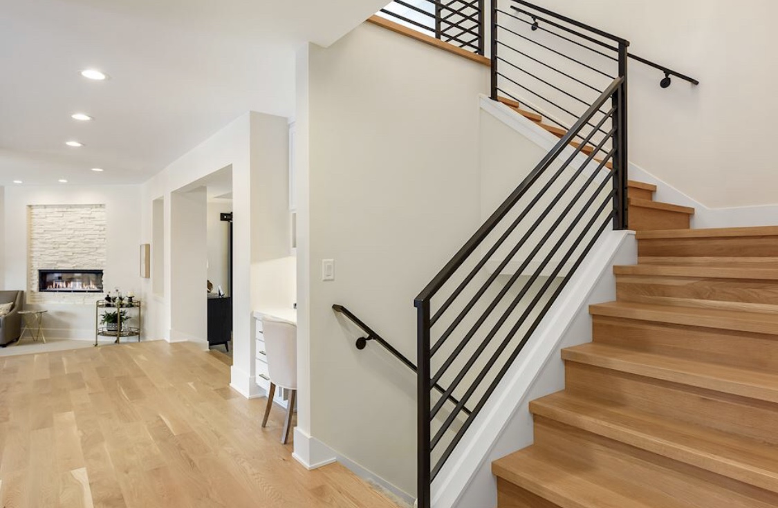 A modern open staircase with a horizontal metal railing and hardwood treads