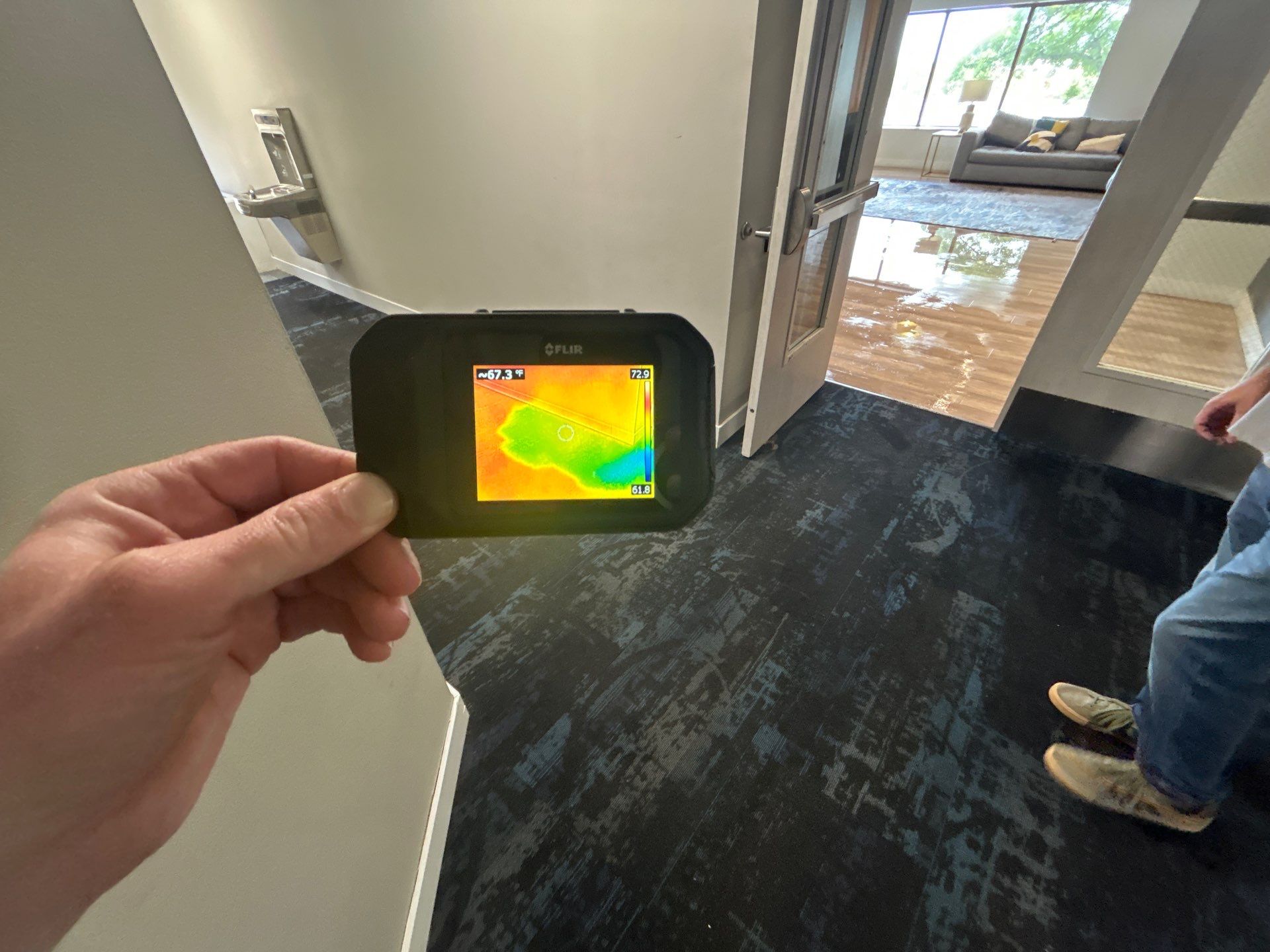 A hand holding a thermal-imaging camera showing a heat map, used to document hidden moisture for an insurance claim