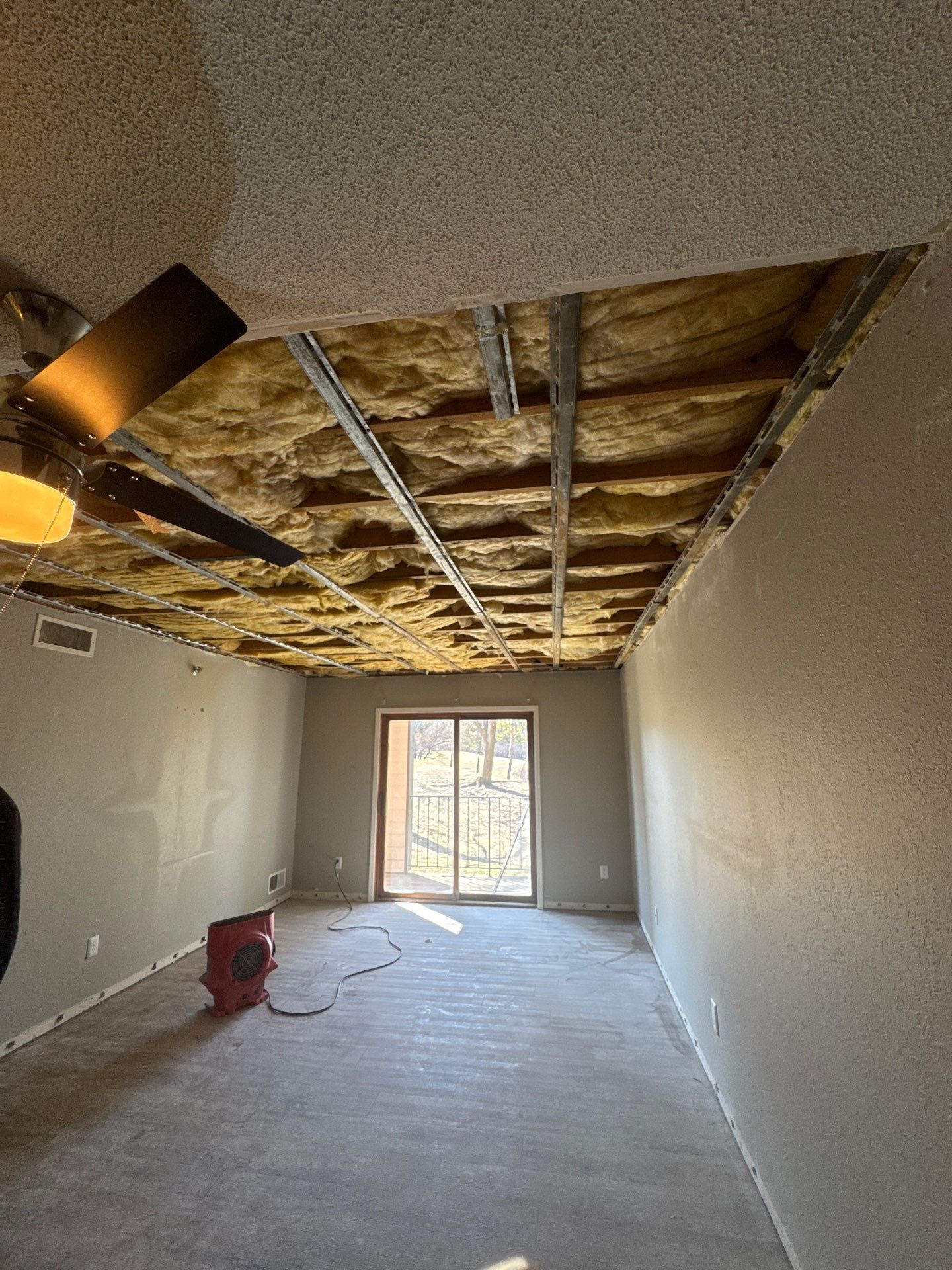 A water-damaged ceiling collapsed to the joists with insulation exposed, before restoration